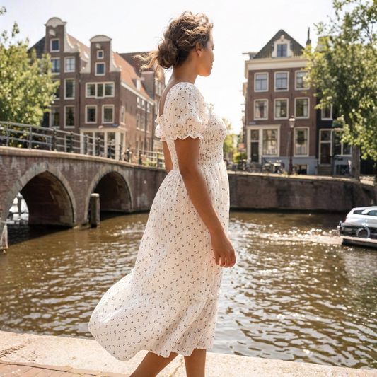 Woman in a white dress standing by a canal with historic buildings in the background
