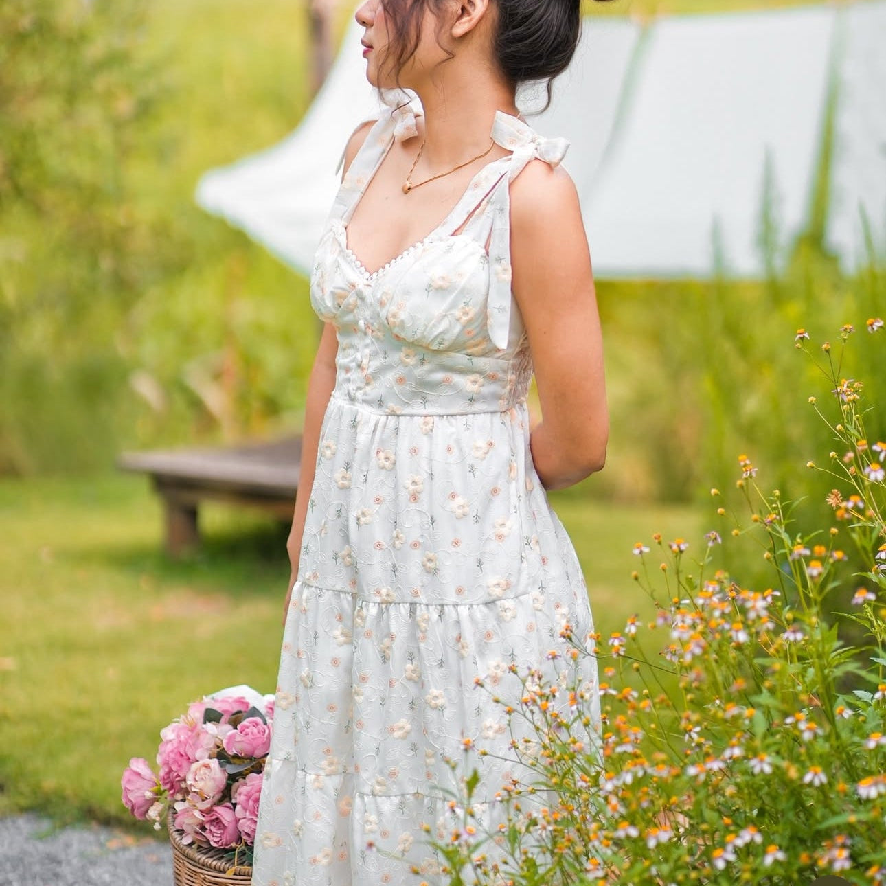 Woman in a light blue floral dress holding flowers in a garden